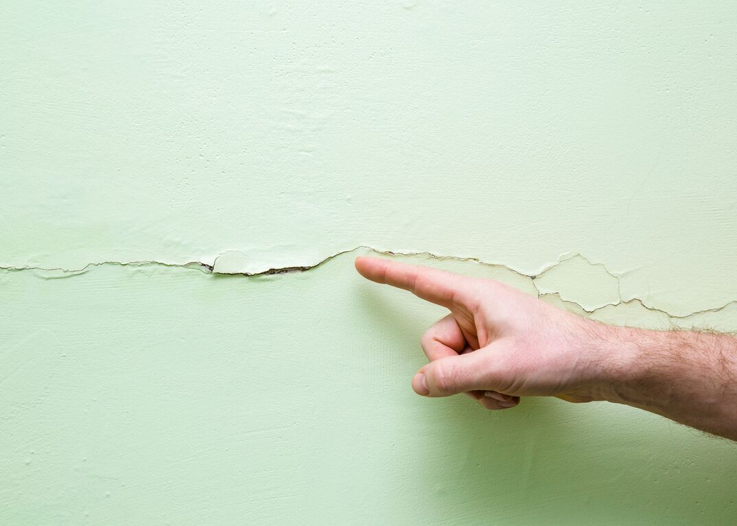 mão apontando para rachadura na parede