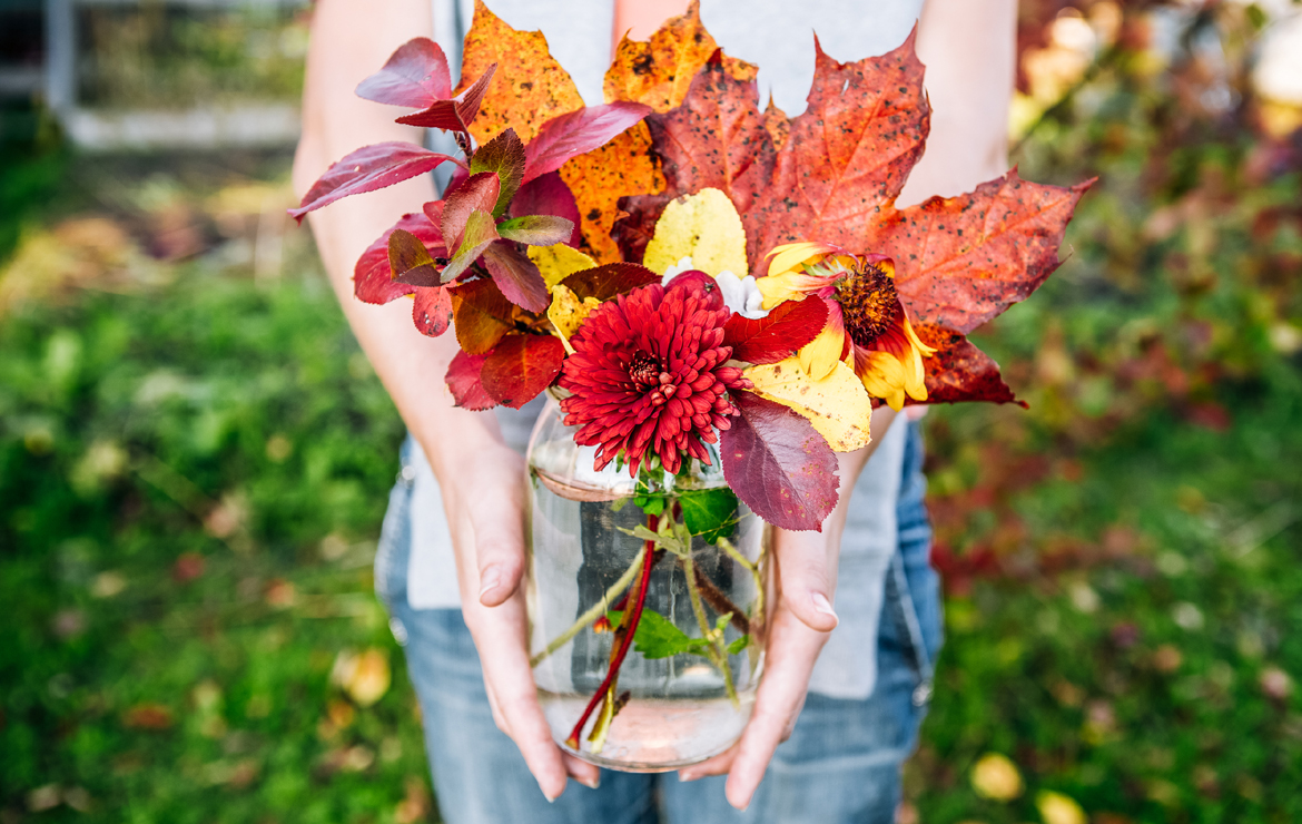 pessoa segurando arranjo de flores com folhas de outono