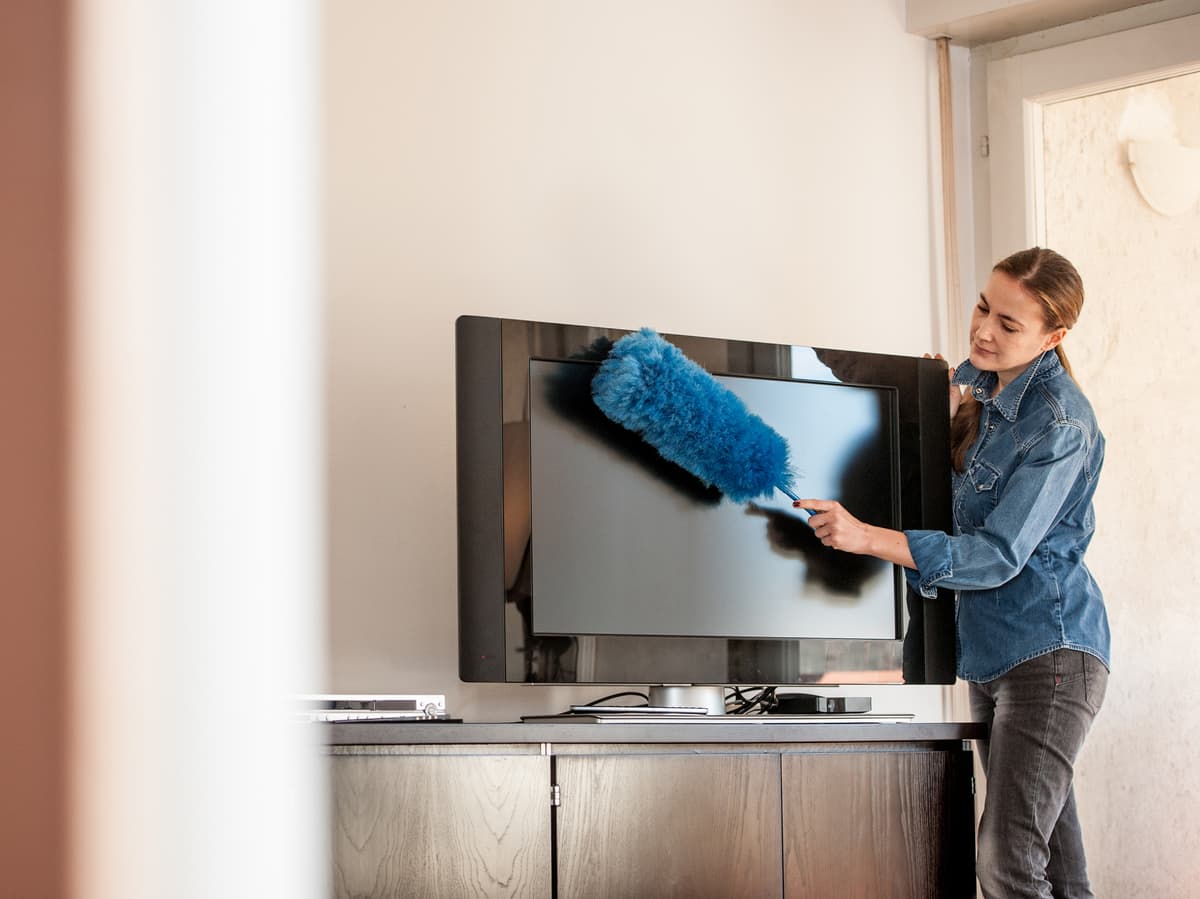 mulher limpando televisão com espanador