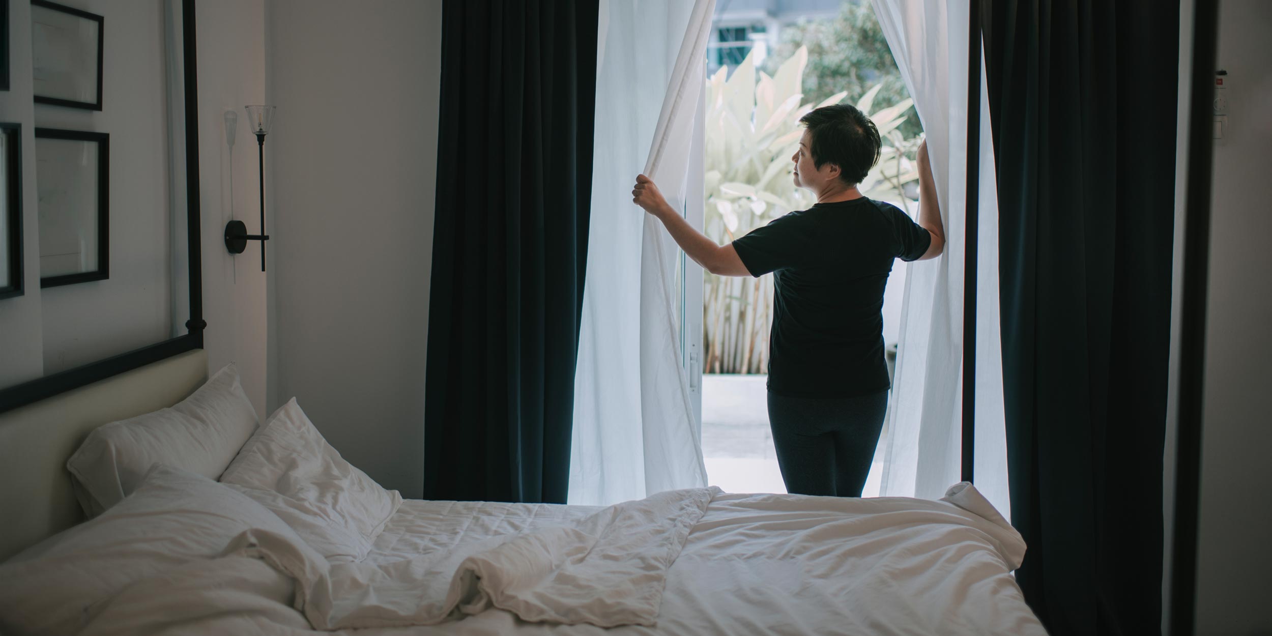 mulher ajeitando cortinas blackout em quarto
