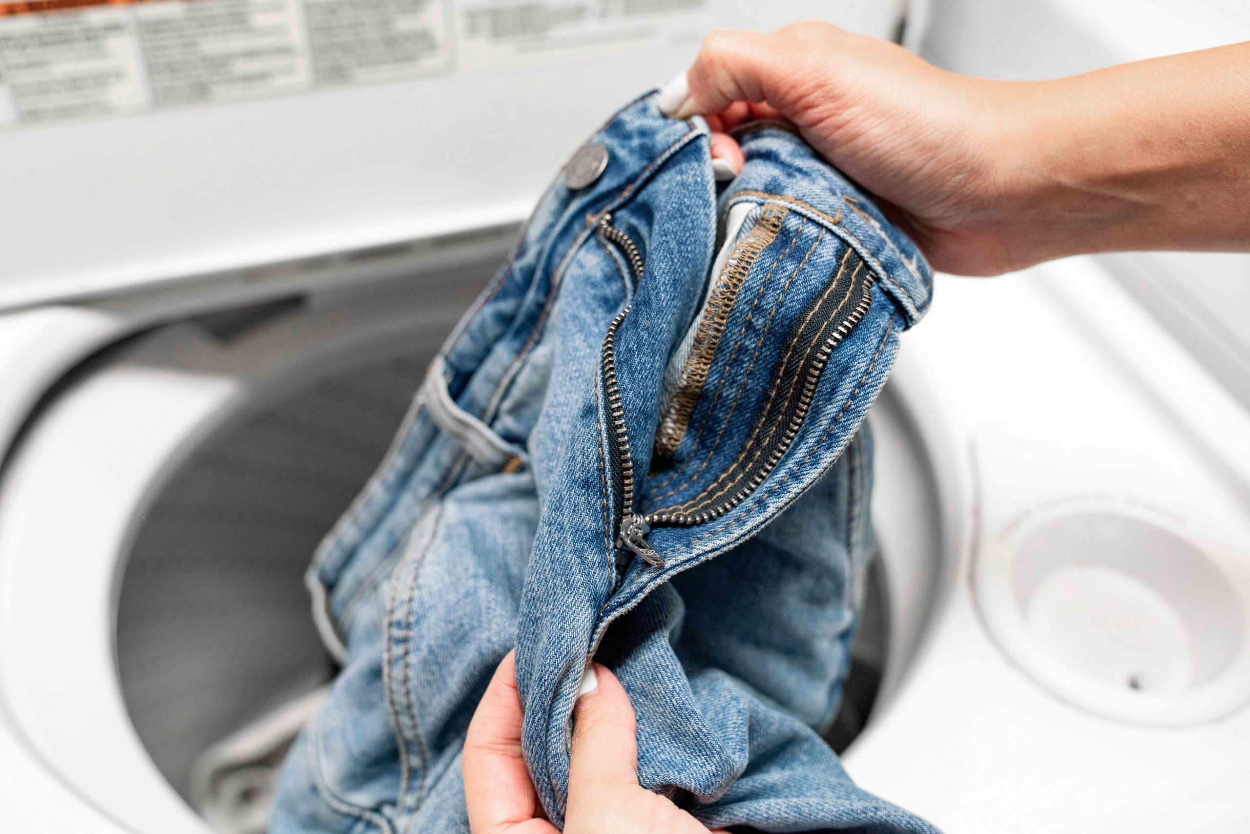 pessoa com calça jeans perto de máquina de lavar