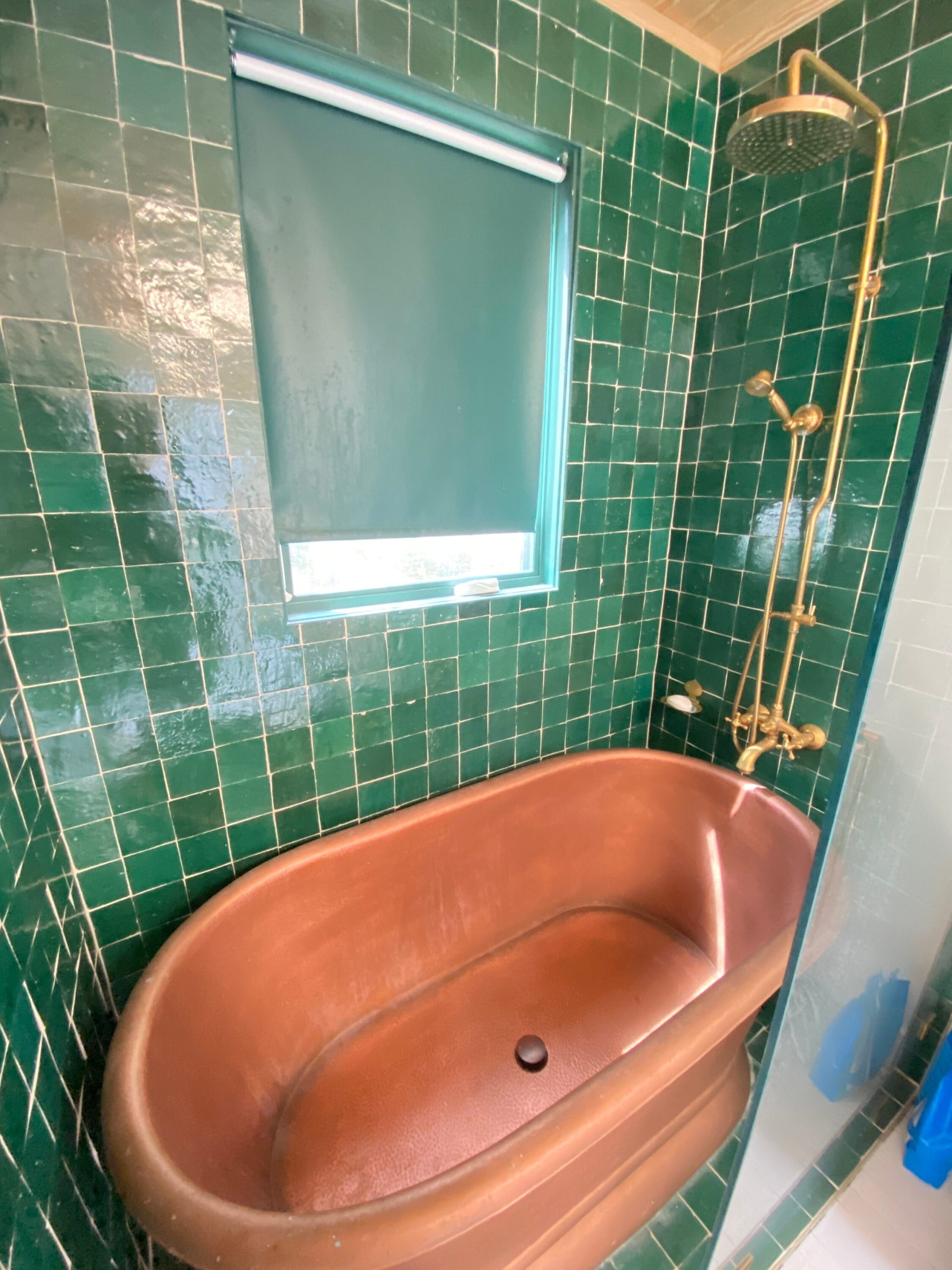 banheiro com azulejos verde-esmeralda e banheira em cor terracota