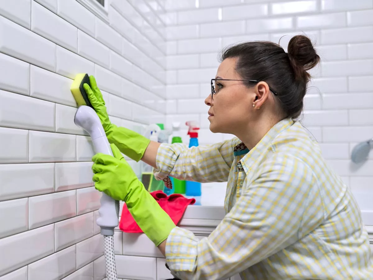 mulher limpando parede de azulejos em banheiro