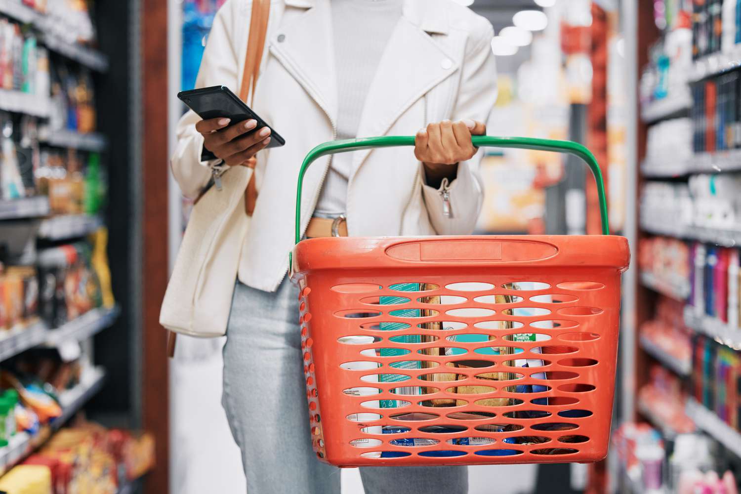 mulher segurando cestinha de supermercado e celular