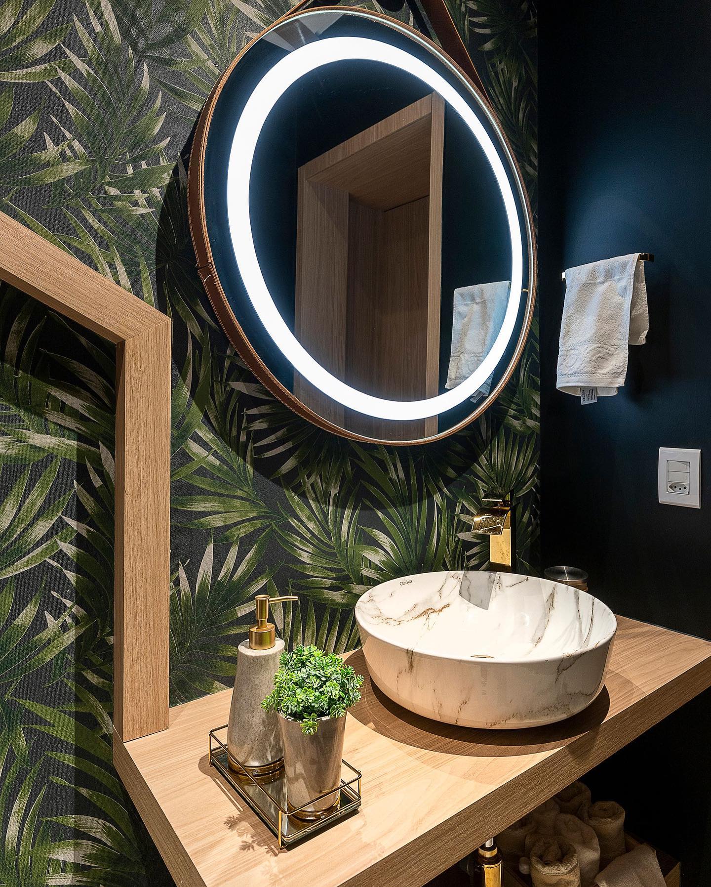 lavabo com papel de parede de folhas e espelho redondo com LED